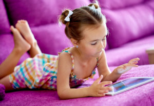 Little girl with a tablet computer o a sofa