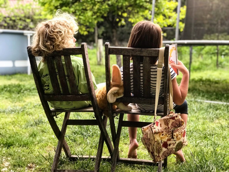 Two Children sitting in chairs outside reading