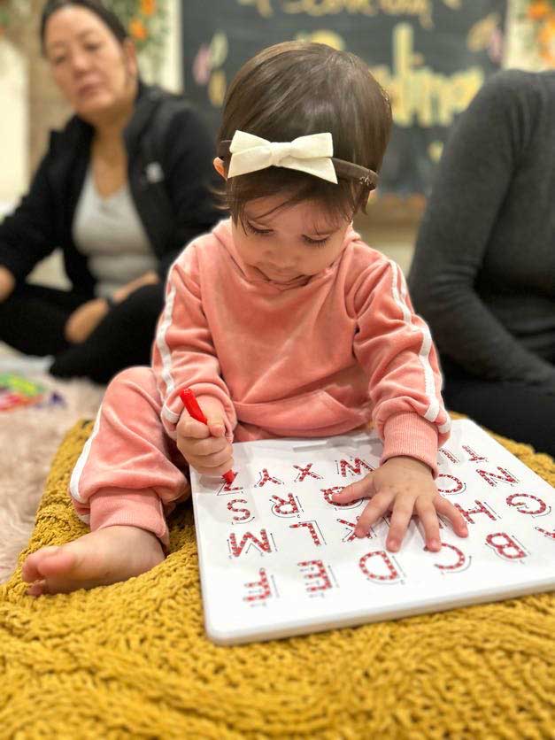 Little girl with a bow in her hair sitting on the floor working on an alphabet sheet
