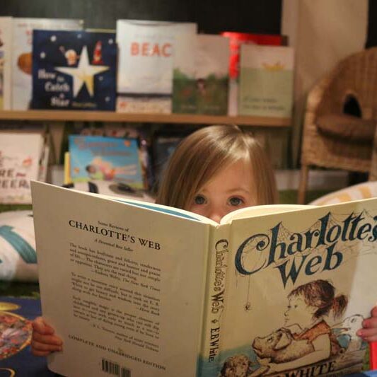 Young girl reading Charlotte's Web in front of a shelf of books