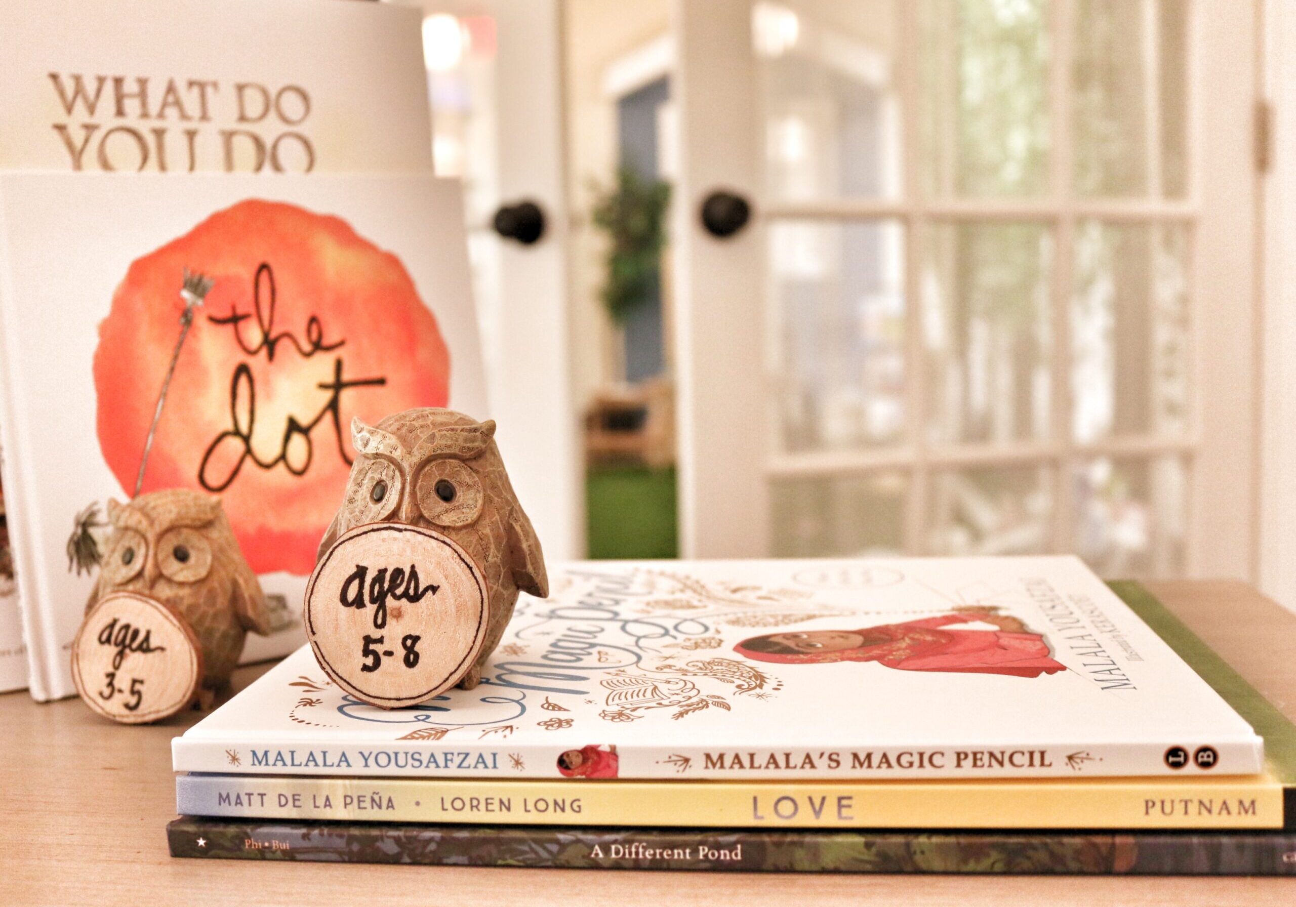Photo of stacked books with a wooden owl on top holding a sig that says "ages 5 - 8"